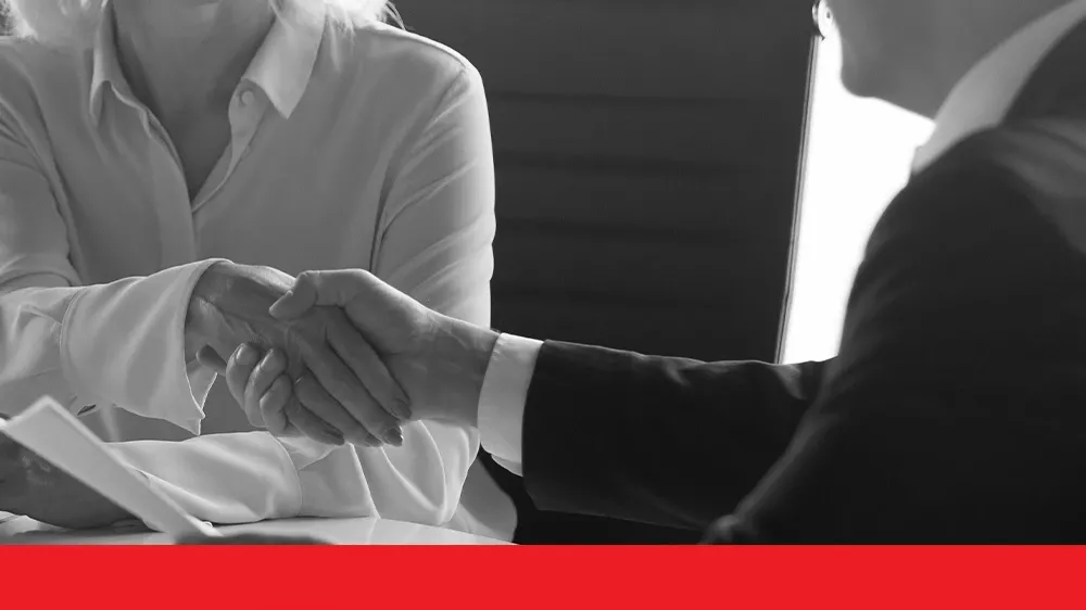 Smiling woman in glasses shaking hands with a man in an office setting.