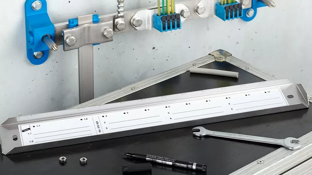 Wall-mounted grounding bar with connected cables above a work case holding a metal rail, wrench, marker, nuts, and cable pieces.