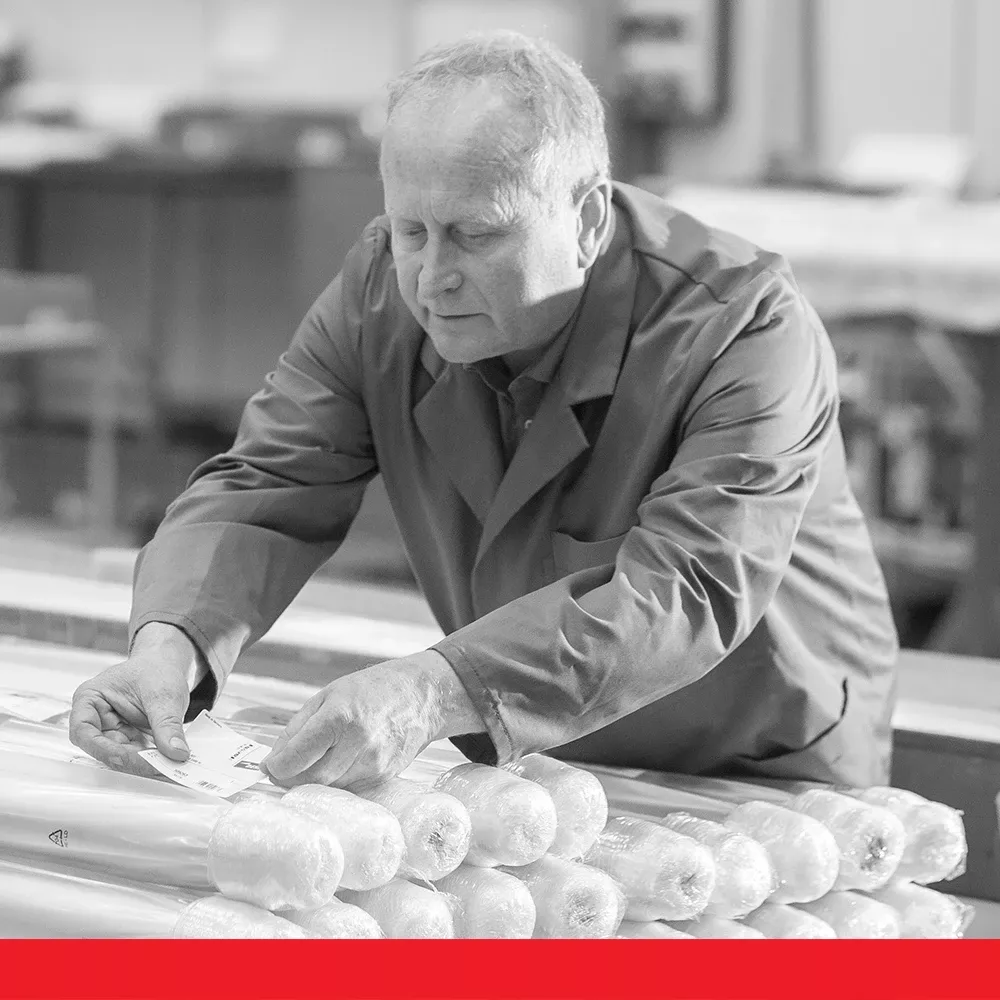Worker in a workshop placing labels on wrapped cylindrical products.
