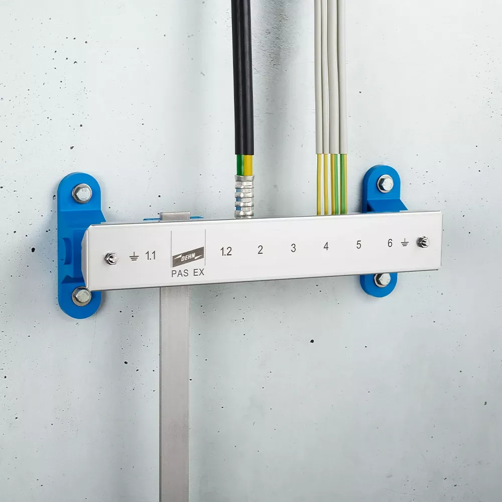 Wall-mounted grounding bar labeled "PAS EX" with numbered terminals and connected cables on a light gray wall.