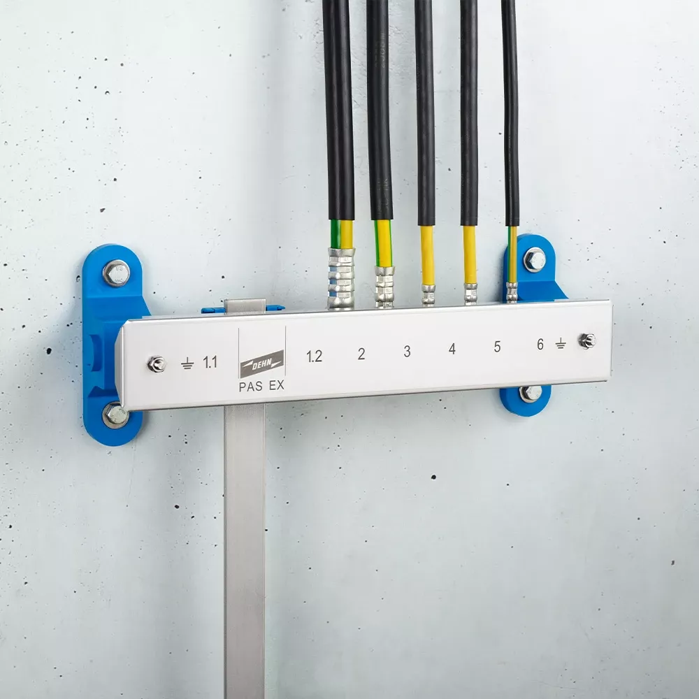 Wall-mounted grounding bar labeled "PAS EX" with numbered terminals and multiple connected black and yellow-green cables.