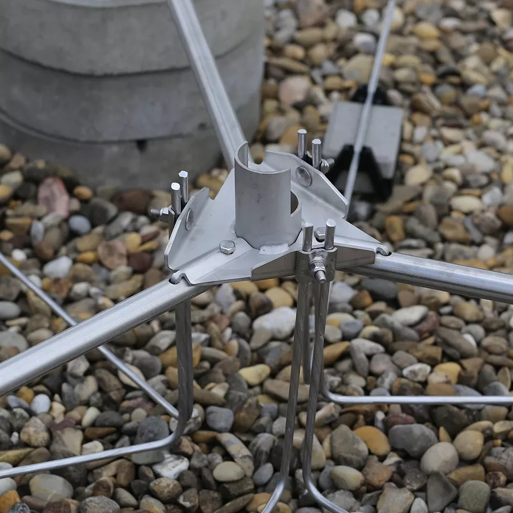 Metal grounding connector joining multiple rods and conductors, mounted on gravel with bolts and clamps visible.