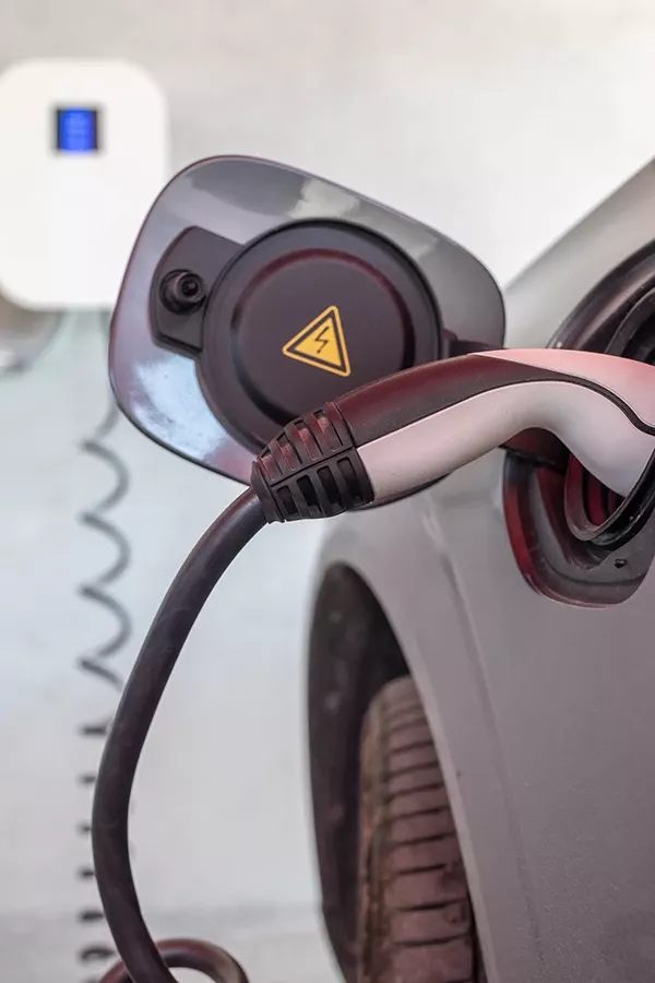 A captivating image displays a sleek electric car charging station, elegantly blending into its garage setting. The clean white wall and the contrasting black-and-white charging cable with a yellow triangle stand out, reflecting modern design and functionality.