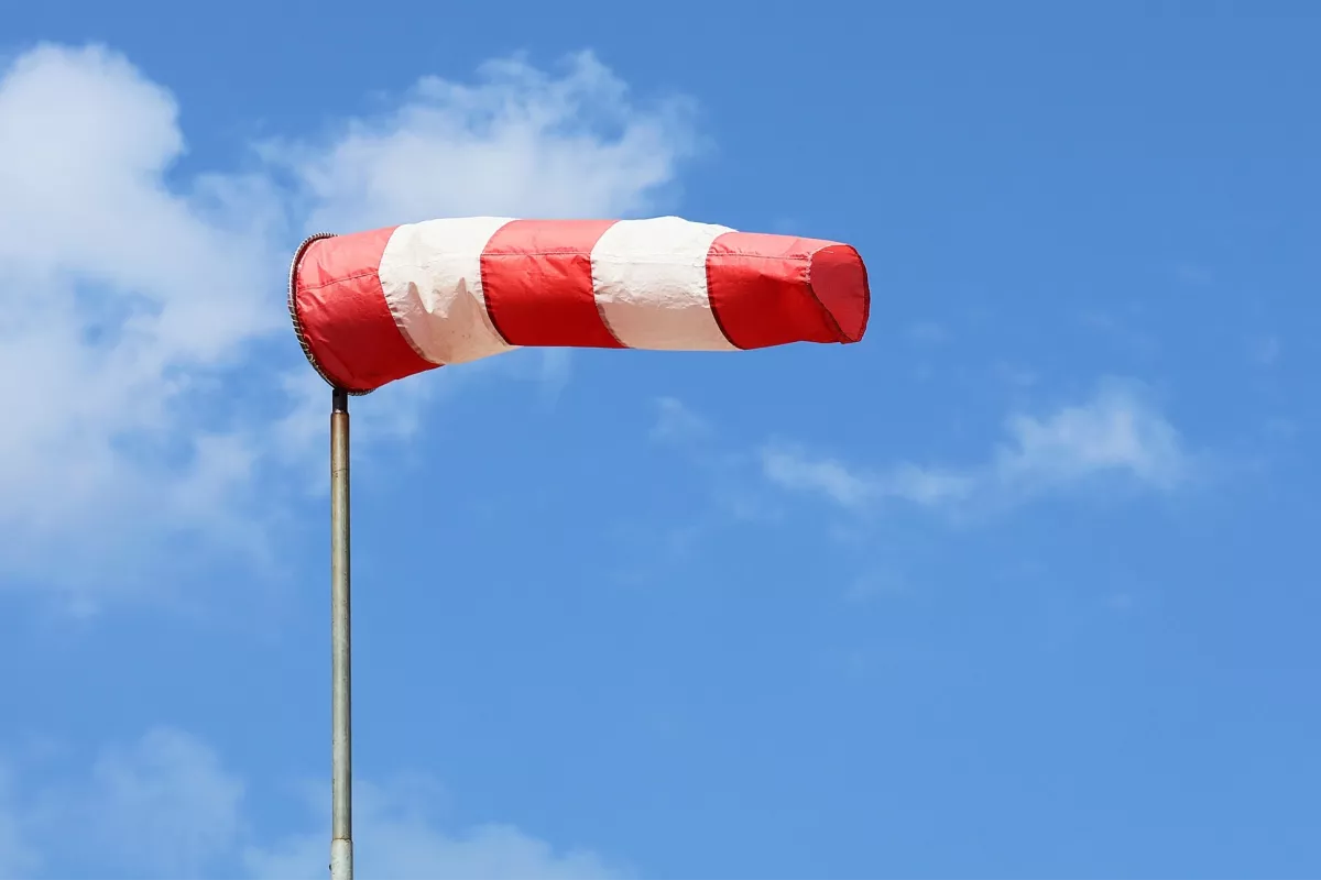 Red and white windsock on a pole against a blue sky with clouds.
