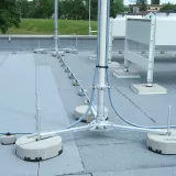A rooftop installation with metal support poles, concrete bases, and visible cables arranged on a flat, gray surface.